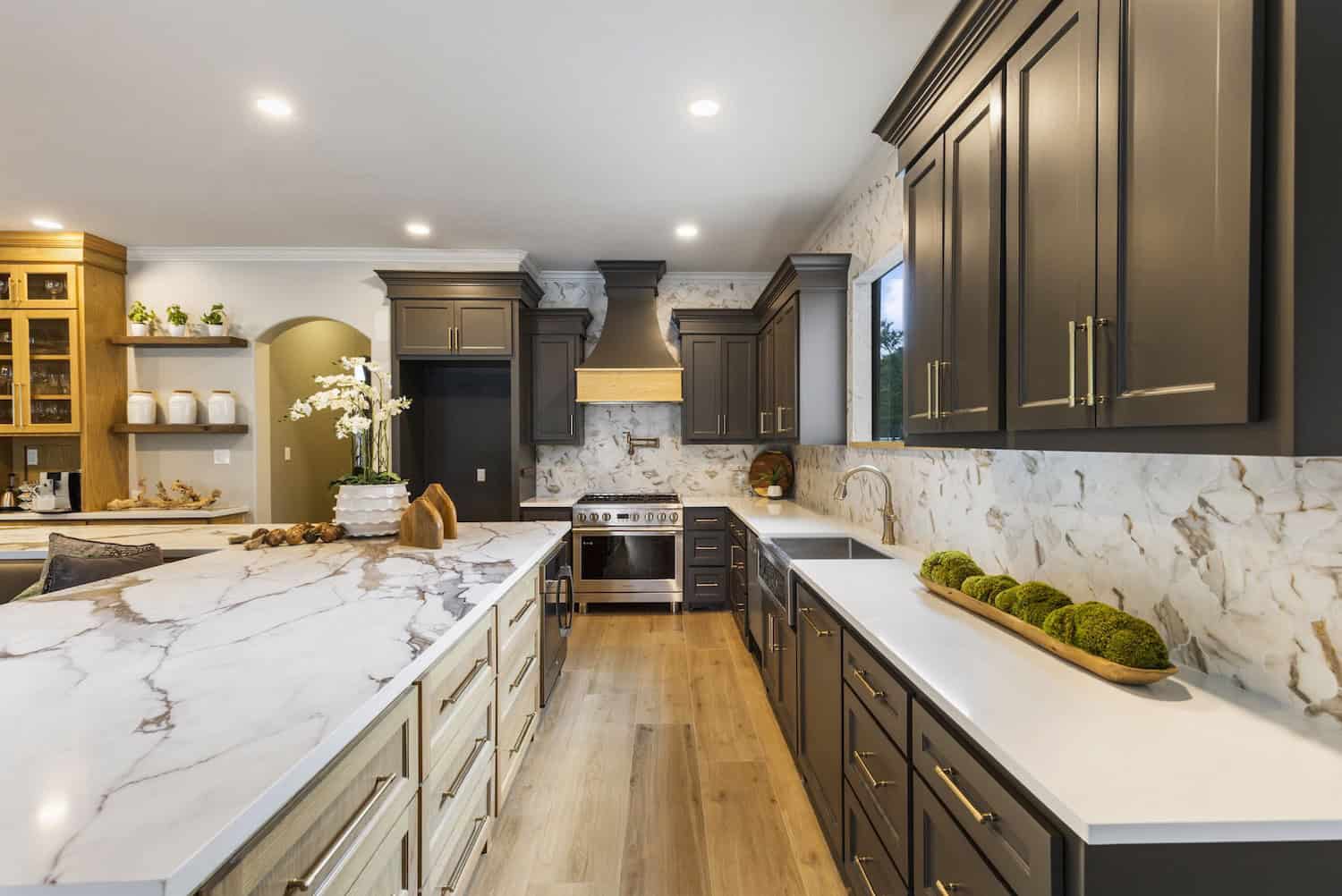 Luxury kitchen with dark cabinets and marble island Stylish modern kitchen with dark wood cabinets, gold hardware, marble backsplash and island, light wood flooring, and stainless steel appliances.