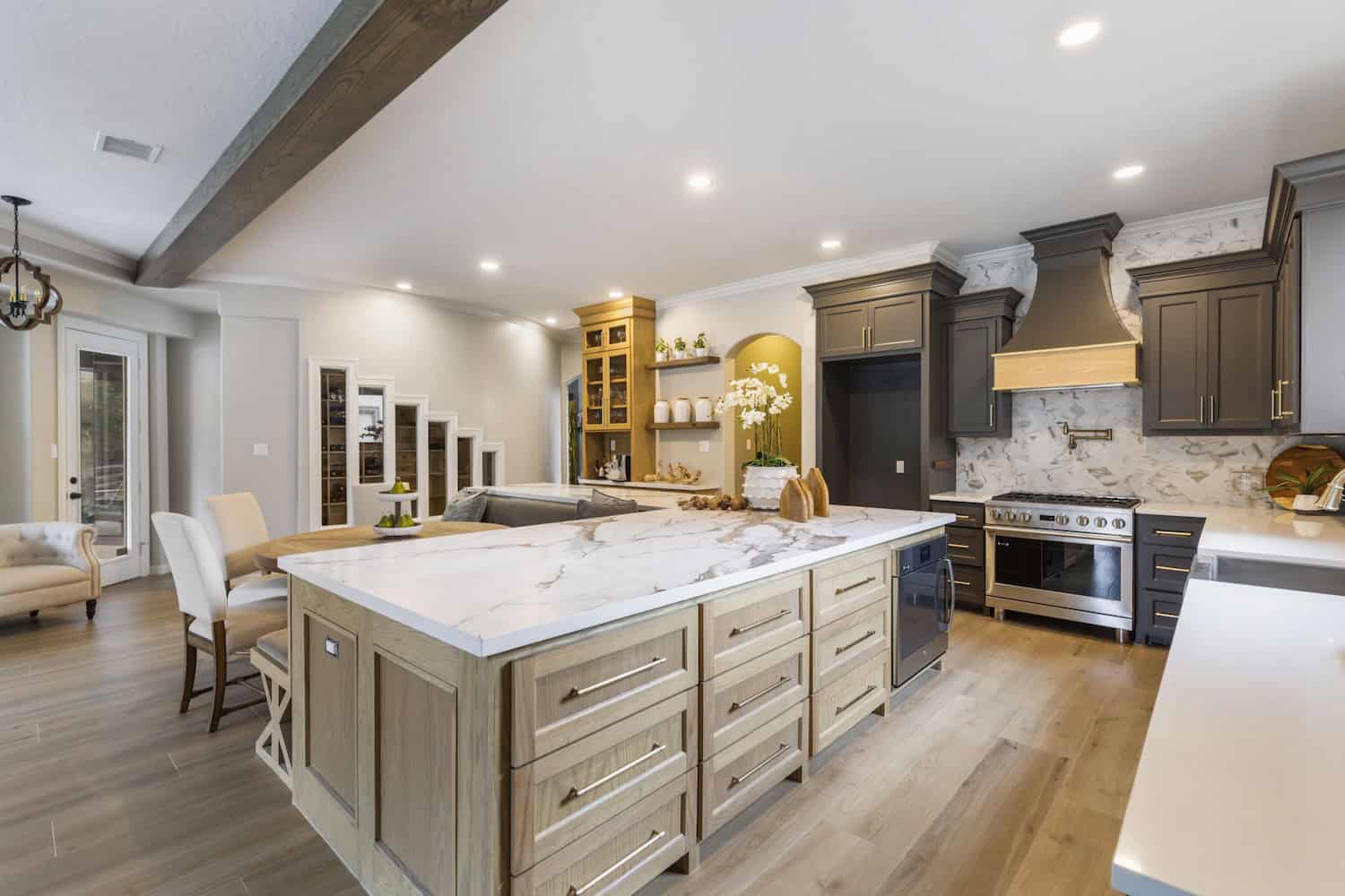 odern kitchen with large marble island, natural wood cabinets, dark upper cabinets, and stainless steel appliances.