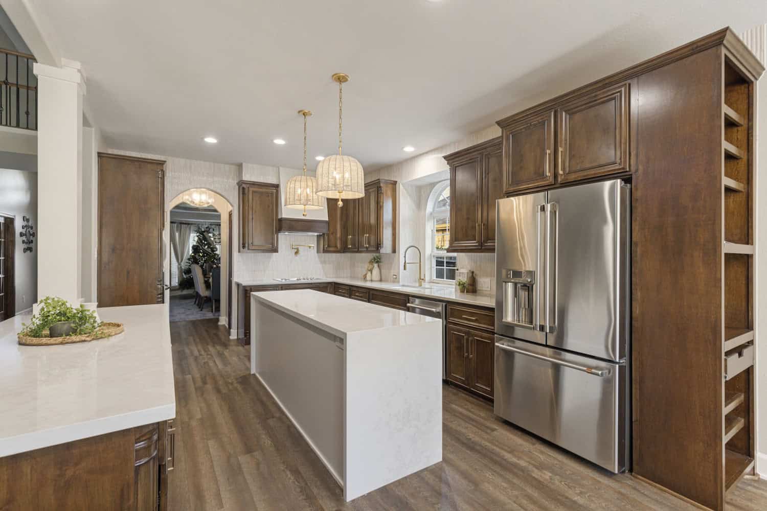 Traditional kitchen with wood cabinets and modern island Warm kitchen design with rich wood cabinets, white quartz island, pendant lighting, stainless steel refrigerator, and hardwood flooring.