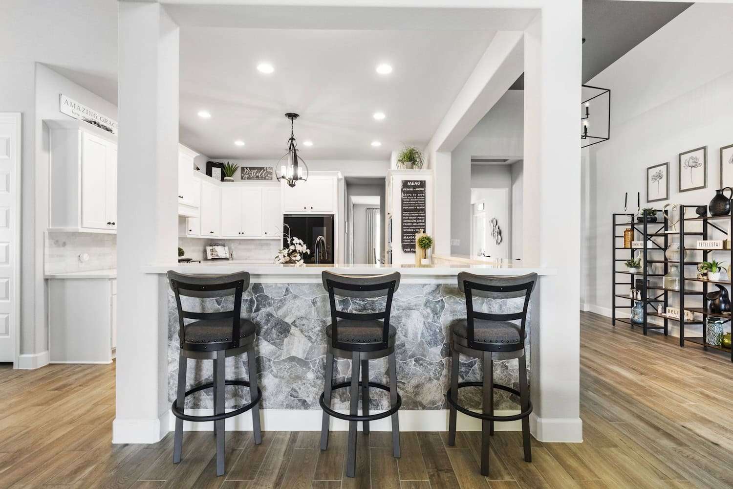 Modern kitchen with stone accent breakfast bar, three black bar stools, and white cabinetry in the background.