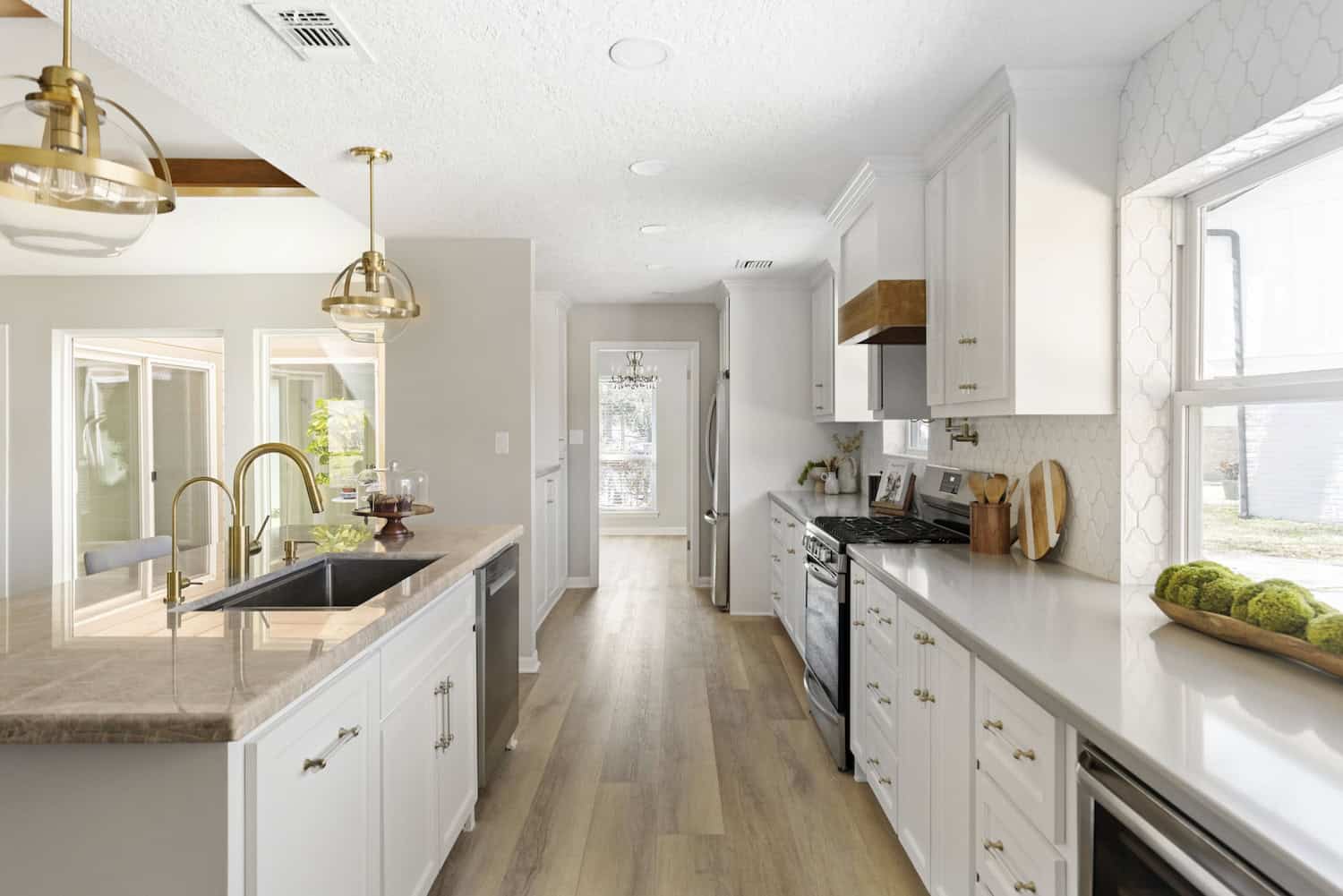 Modern white kitchen with gold accents Bright modern kitchen with white cabinets, wood flooring, gold pendant lights, and stainless steel appliances.