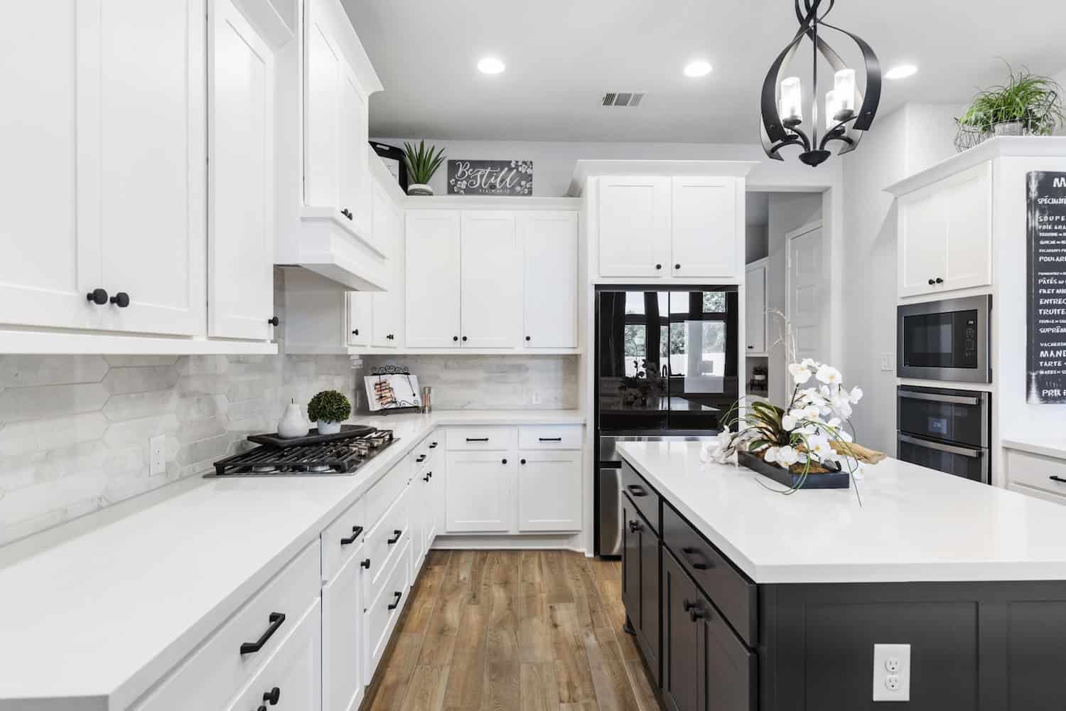 Stylish kitchen with white cabinets, black island, wood flooring, quartz countertops, and modern chandelier lighting.