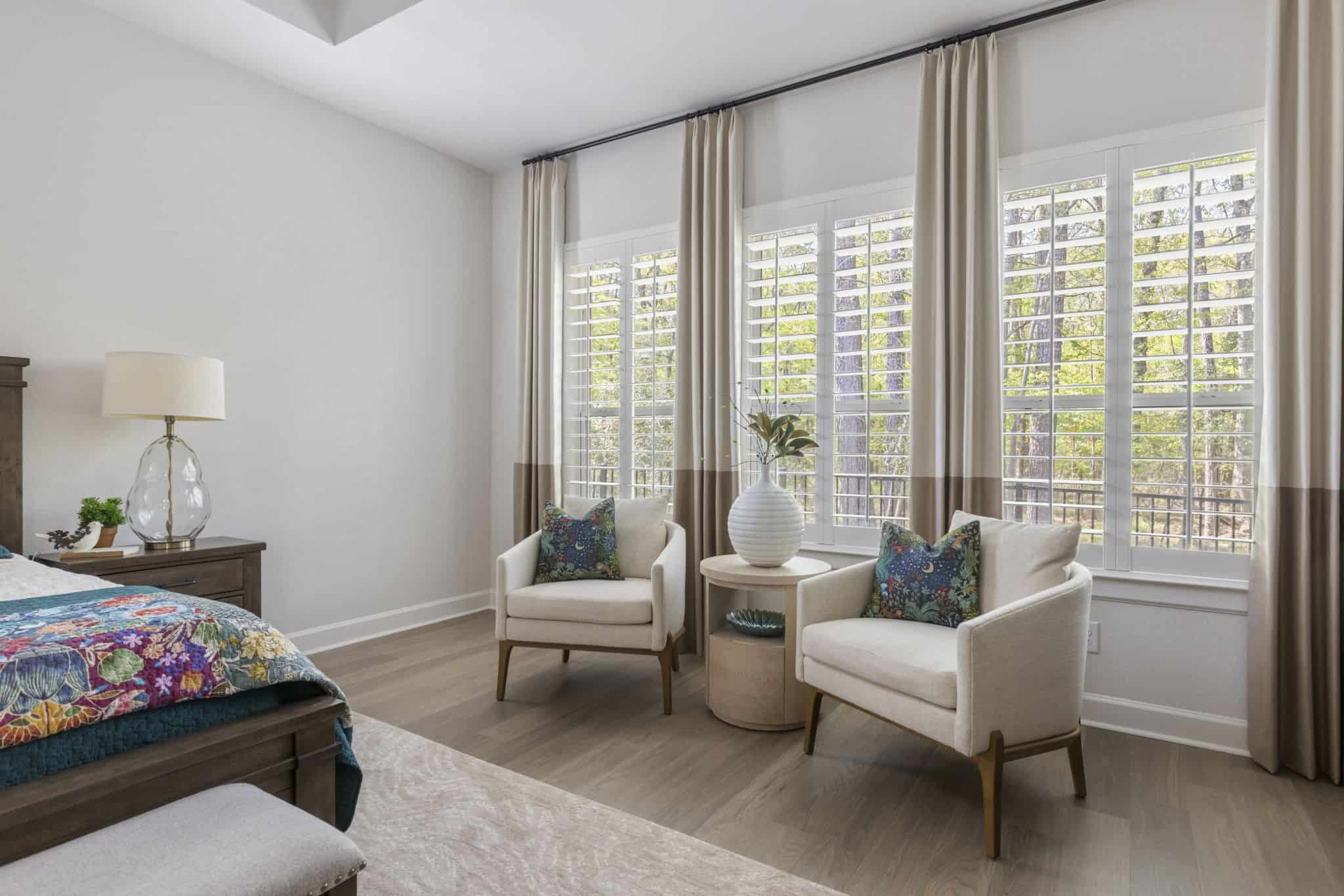 Bright and elegant bedroom seating area with natural light and soft tones Cozy bedroom corner with two armchairs by large windows and neutral curtains