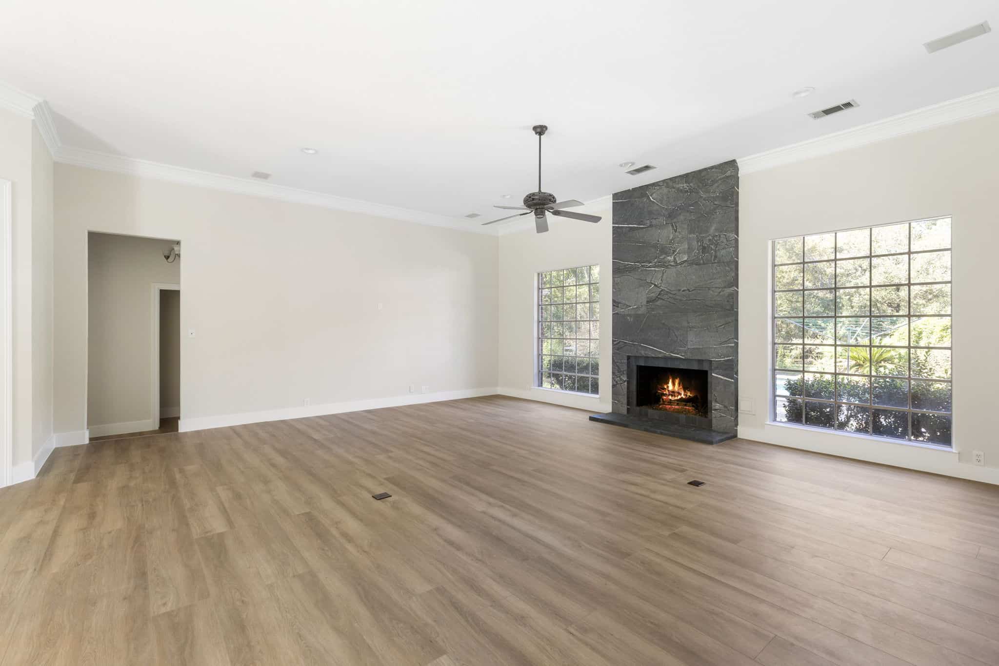 Open living space with hardwood flooring and modern fireplace Spacious living room with wooden floors, fireplace, and ceiling fan