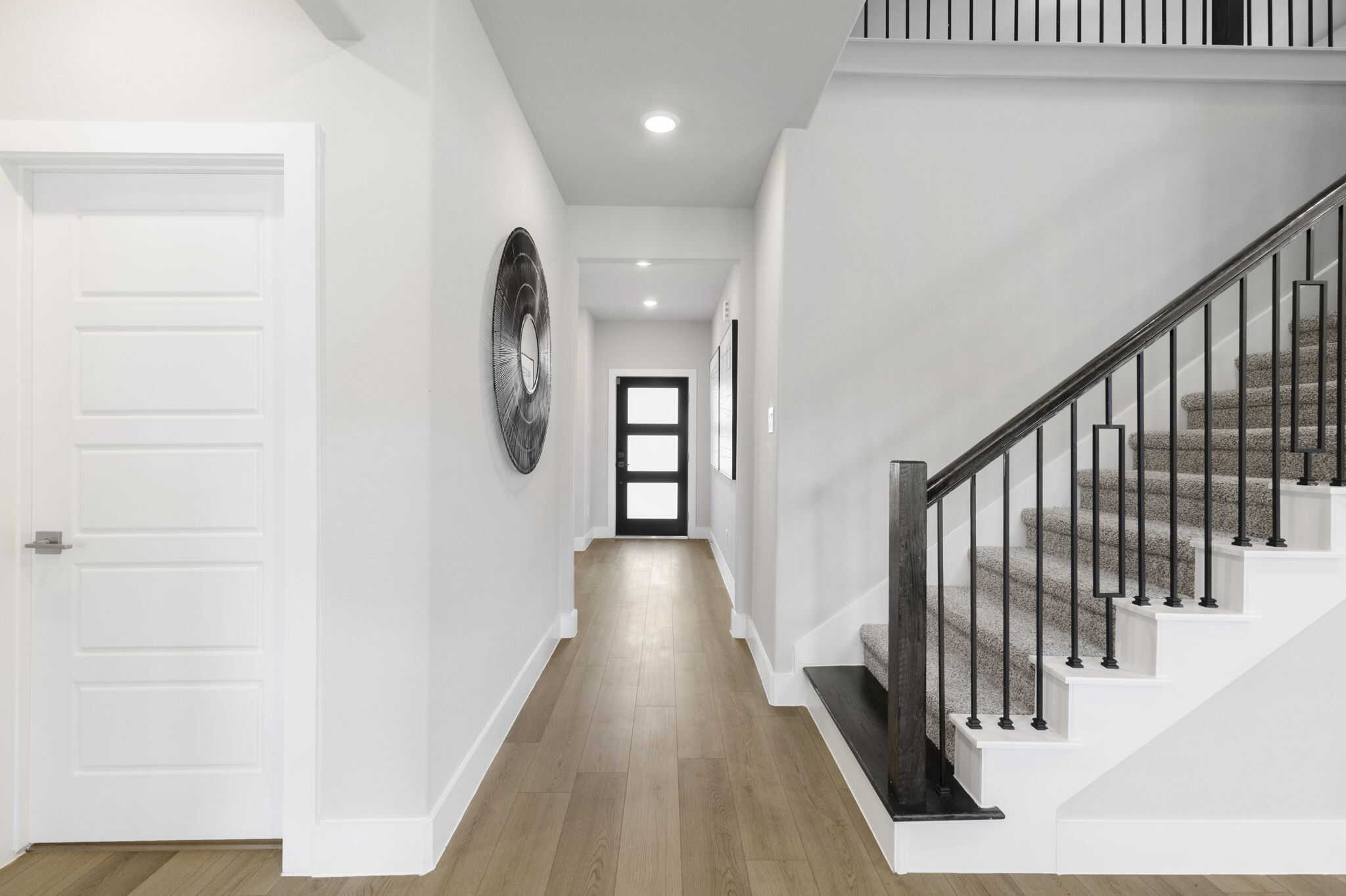 Contemporary foyer featuring wood flooring and minimalist design Bright entryway with staircase and modern black railing