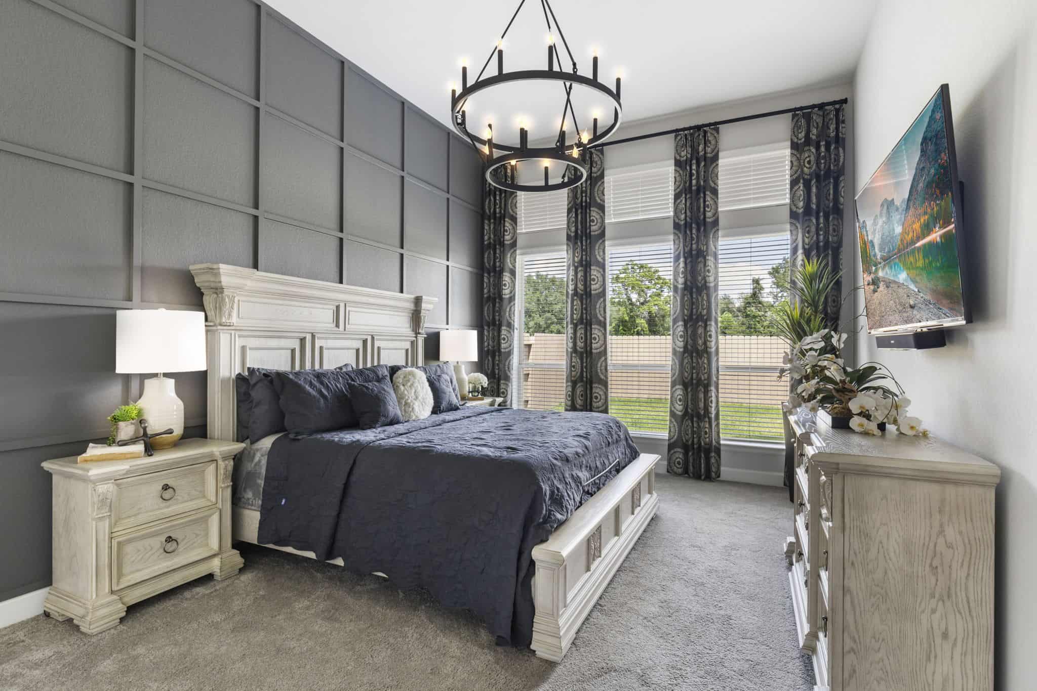 Primary bedroom with custom patterned drapery panels, upholstered bed, and modern chandelier