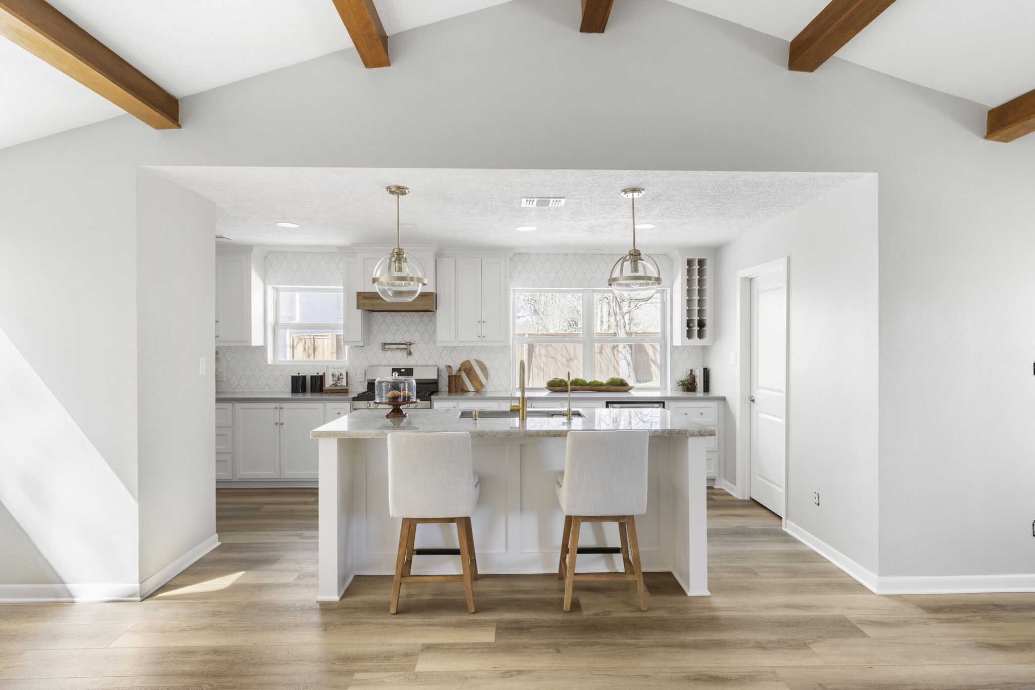Bright white kitchen with island seating, pendant lights, and exposed wood ceiling beams