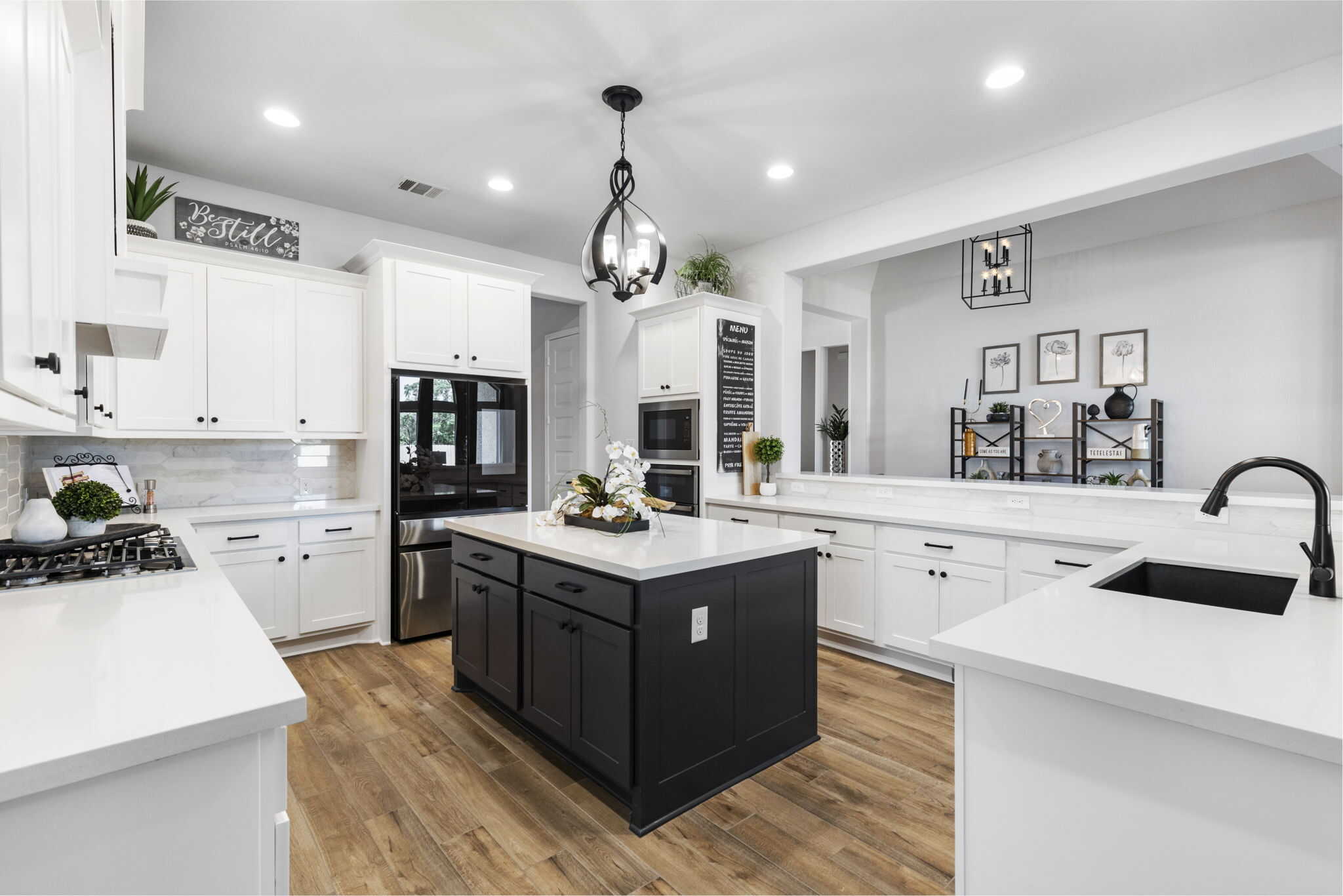 Modern white kitchen with black island, stainless steel appliances, and pendant lighting
