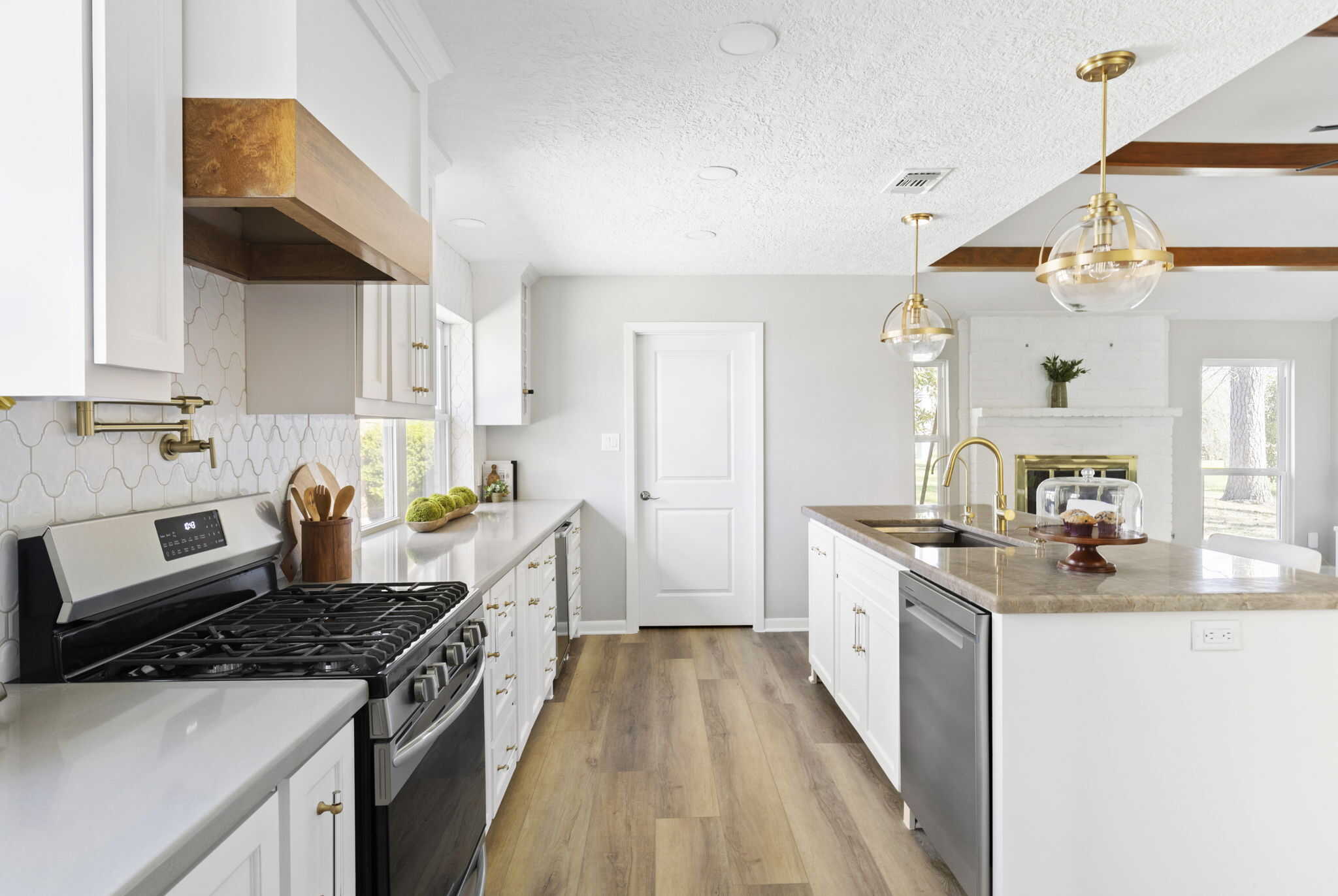 Bright white kitchen with gas range, wood vent hood, white island, brass fixtures, and pendant lighting