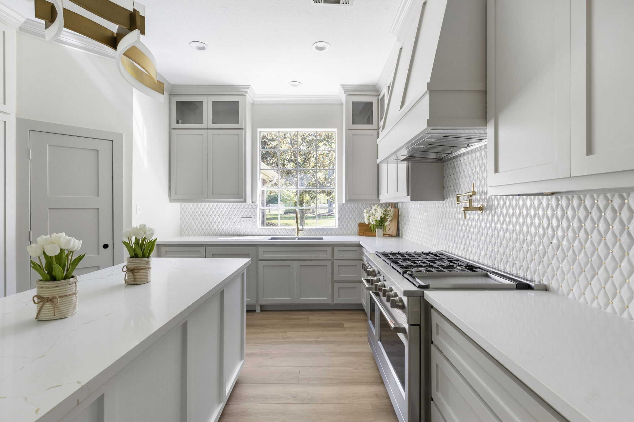 Modern kitchen with light gray cabinets, white island, gas range, textured backsplash, and brass accents
