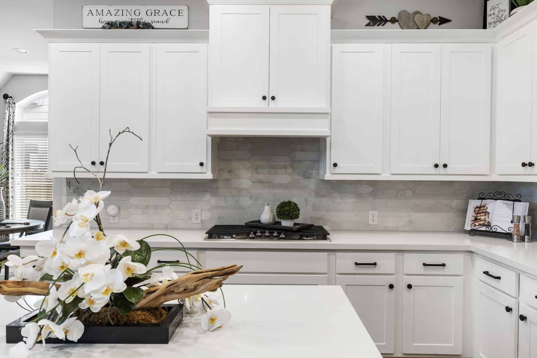 White kitchen with shaker cabinets, gas cooktop, light stone backsplash, and decorative island centerpiece