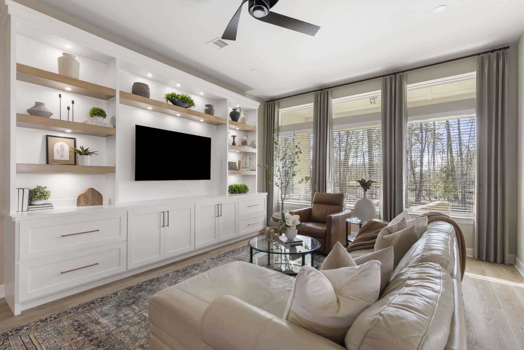 Living room with built-in shelving, wall-mounted TV, sofa, and large windows