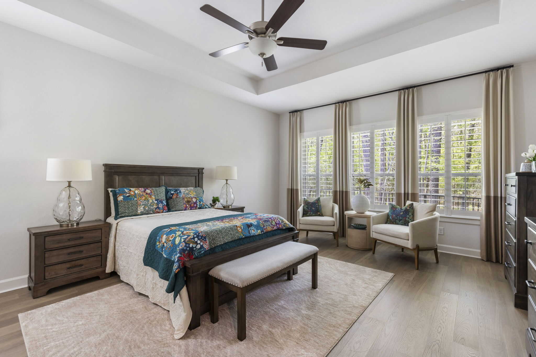 Bedroom with wooden bed frame, bench, seating area, and large windows