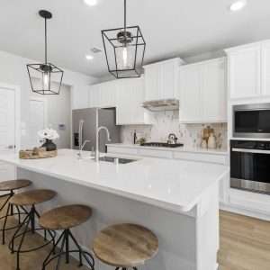 After Renovation – Modern White Kitchen with Island Bright modern kitchen after renovation with white cabinets, large island, bar stools, pendant lighting, and stainless steel appliances