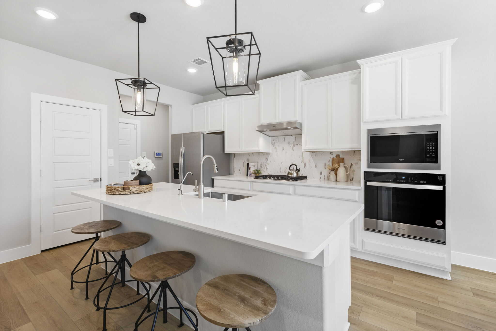Bright modern kitchen after renovation with white cabinets, large island, bar stools, pendant lighting, and stainless steel appliances