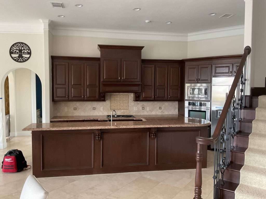 Kitchen before renovation with dark wood cabinets, large island, granite countertops, and built-in stainless steel appliances