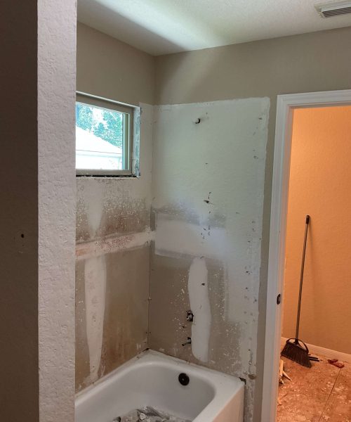 Bathroom renovation in progress with bathtub area partially demolished, exposed walls, and visible plumbing fixtures