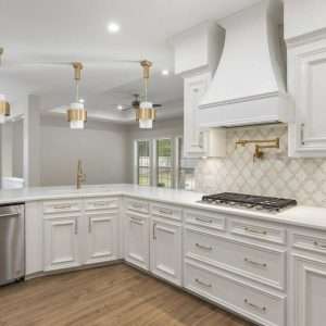 Open-concept kitchen with white cabinets, gold hardware, large island, and patterned tile backsplash