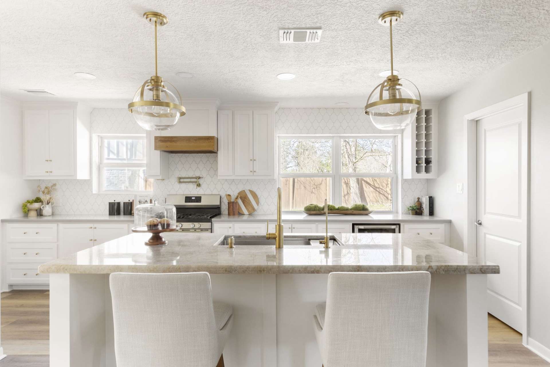 White kitchen remodel with brass globe pendants and waterfall stone island
