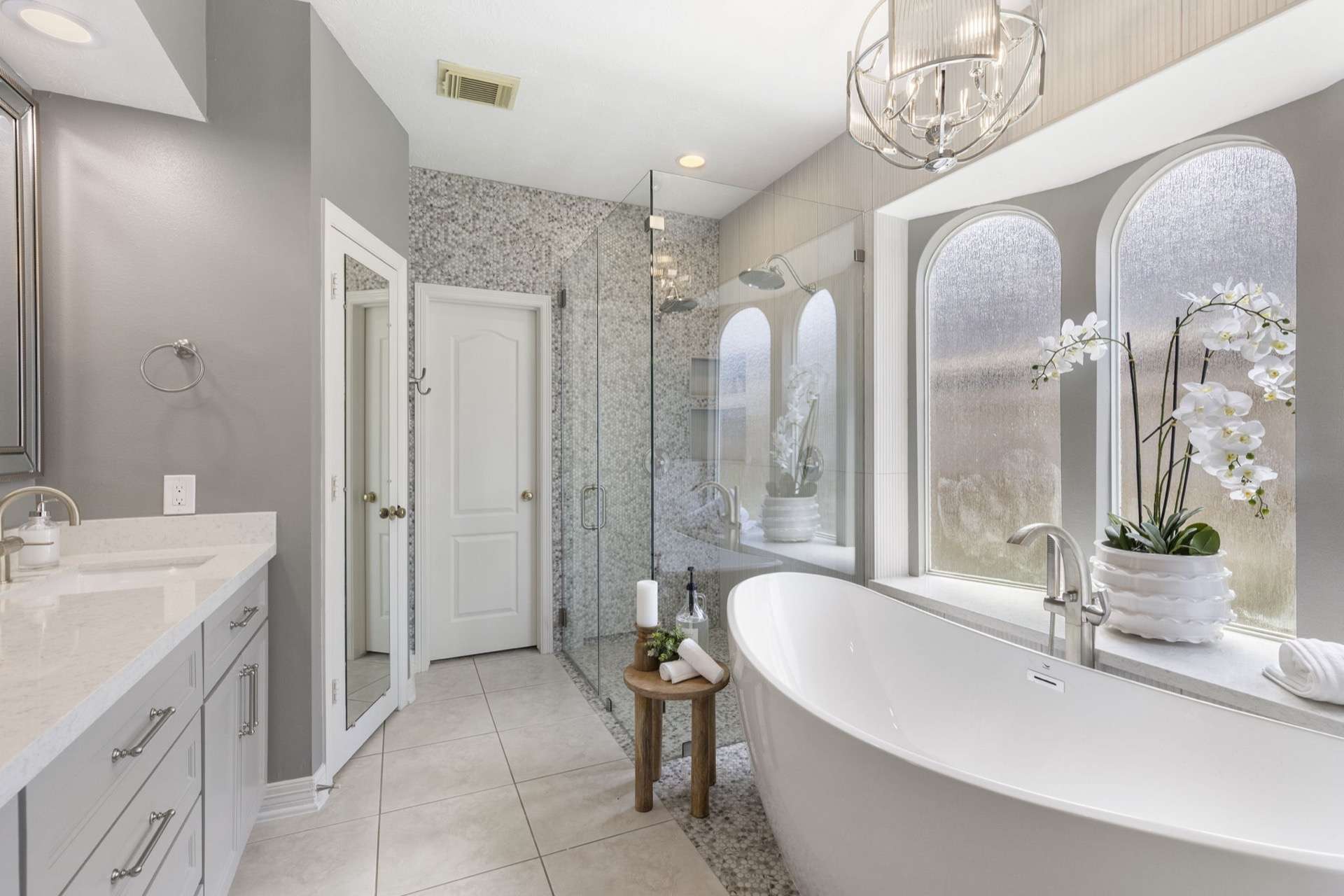 Luxury primary bath with freestanding tub under arched windows and a chandelier